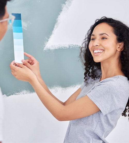 Woman holding paint swatches up to a partially painted wall
